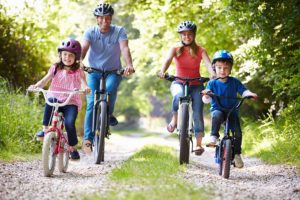 Family with mom, dad, female child and male child riding bicycles down a bike path.