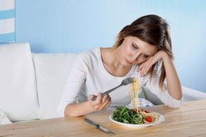 Image of caucasian woman struggling with depression while looking at a plate of food.