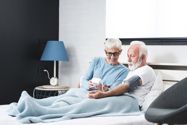 Senior couple in pajamas in a bed in a bedroom measure each other's blood pressure