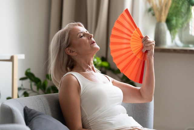 Stressed old senior woman using fan suffer from overheating