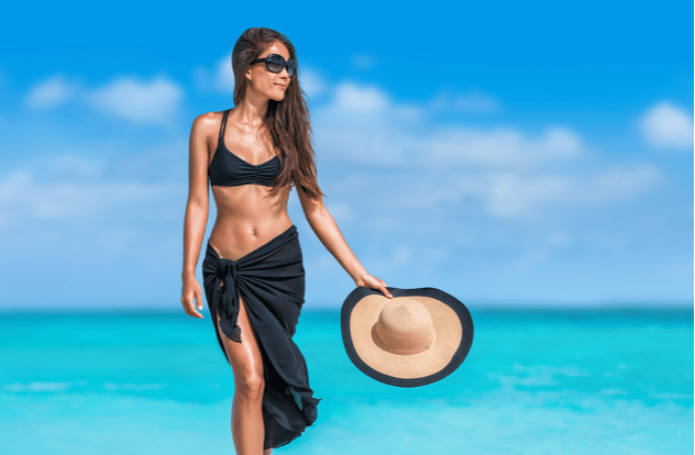 Elegant beach woman in bikini and fashion sarong standing on shore.