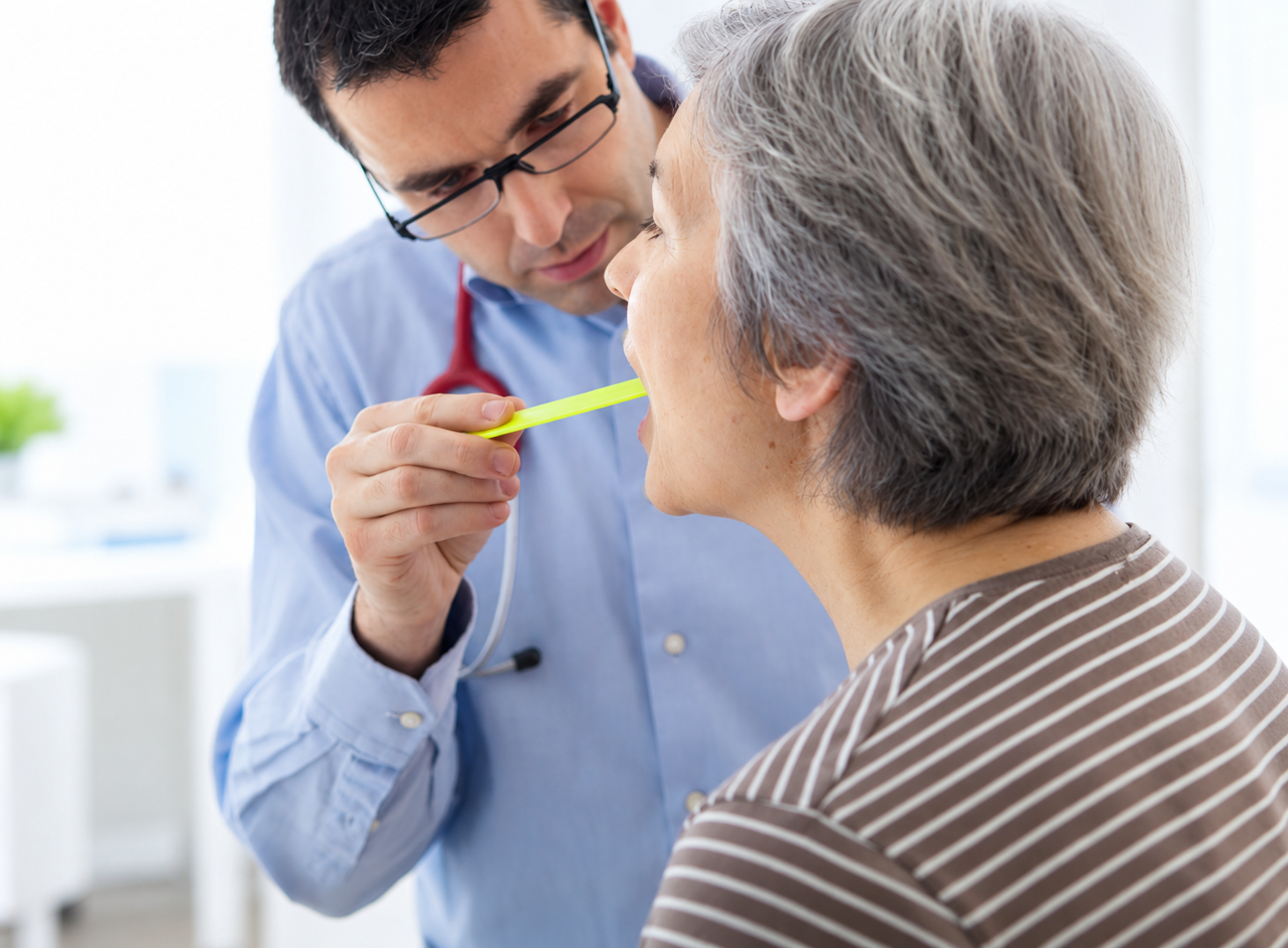 Woman is examined by doctor with a tongue depressor.